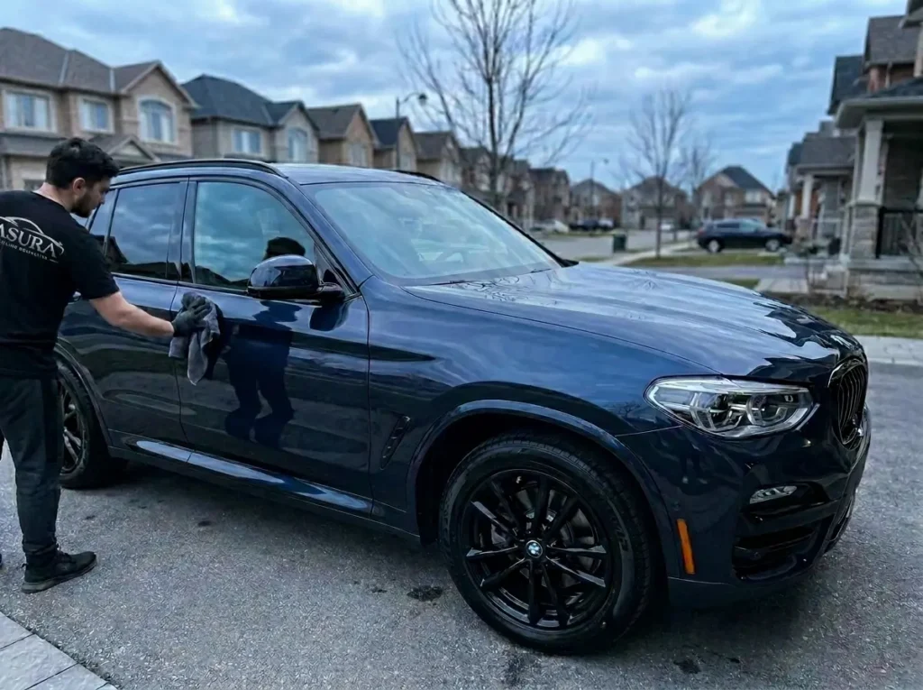 Detailer wiping and finishing the exterior panel of a black vehicle during mobile car detailing